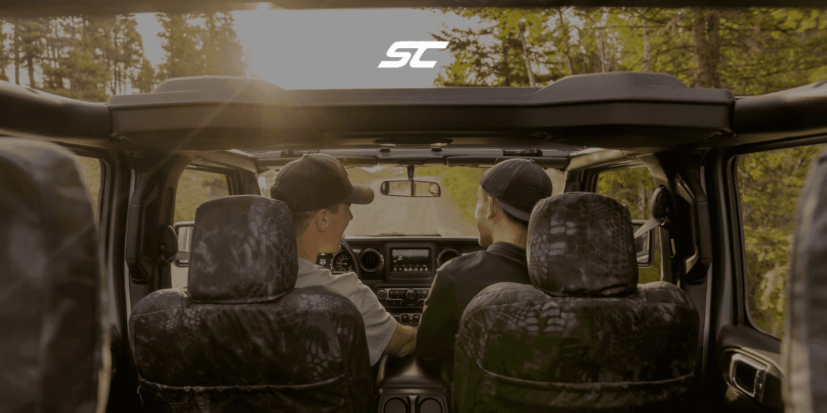 Two individuals enjoying a scenic drive in an off-road vehicle with the roof down, showcasing a serene outdoor adventure with a focus on the landscape ahead.