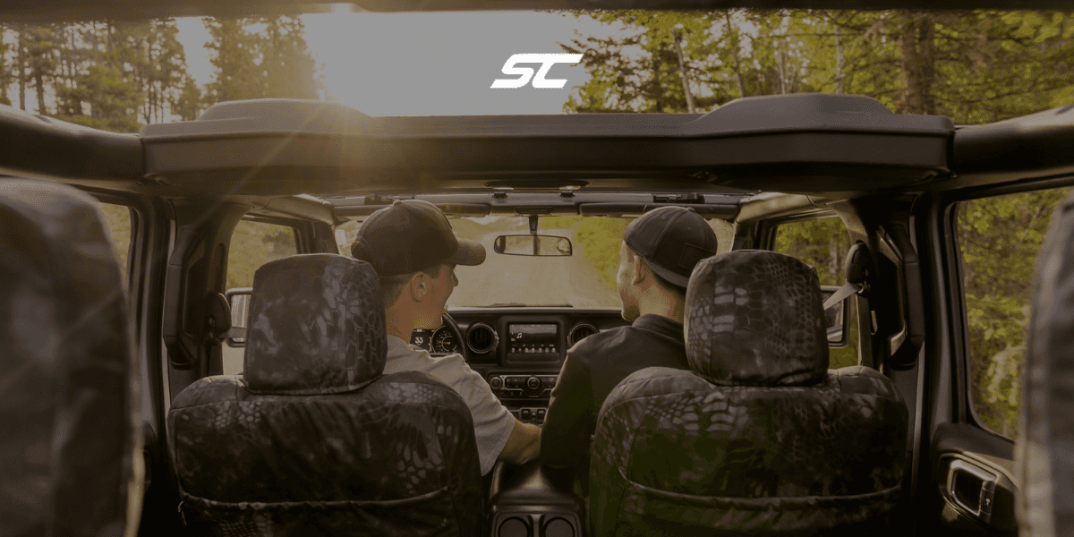 Two individuals enjoying a scenic drive in an off-road vehicle with the roof down, showcasing a serene outdoor adventure with a focus on the landscape ahead.