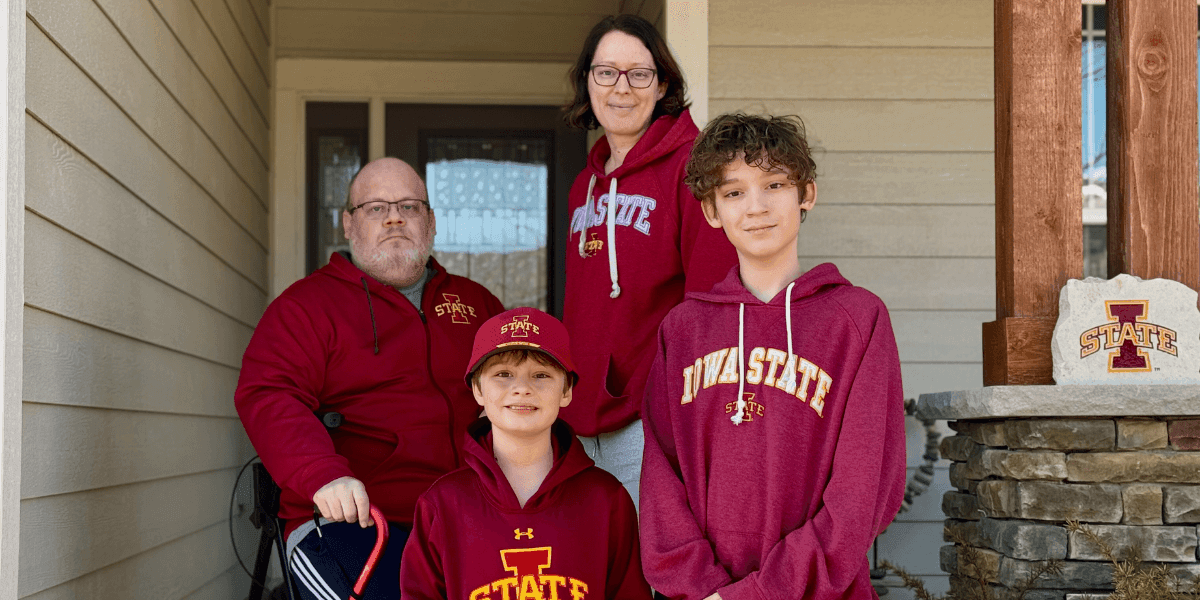 A family of four wearing Iowa State apparel, standing together on a porch with a welcoming, community-focused atmosphere.