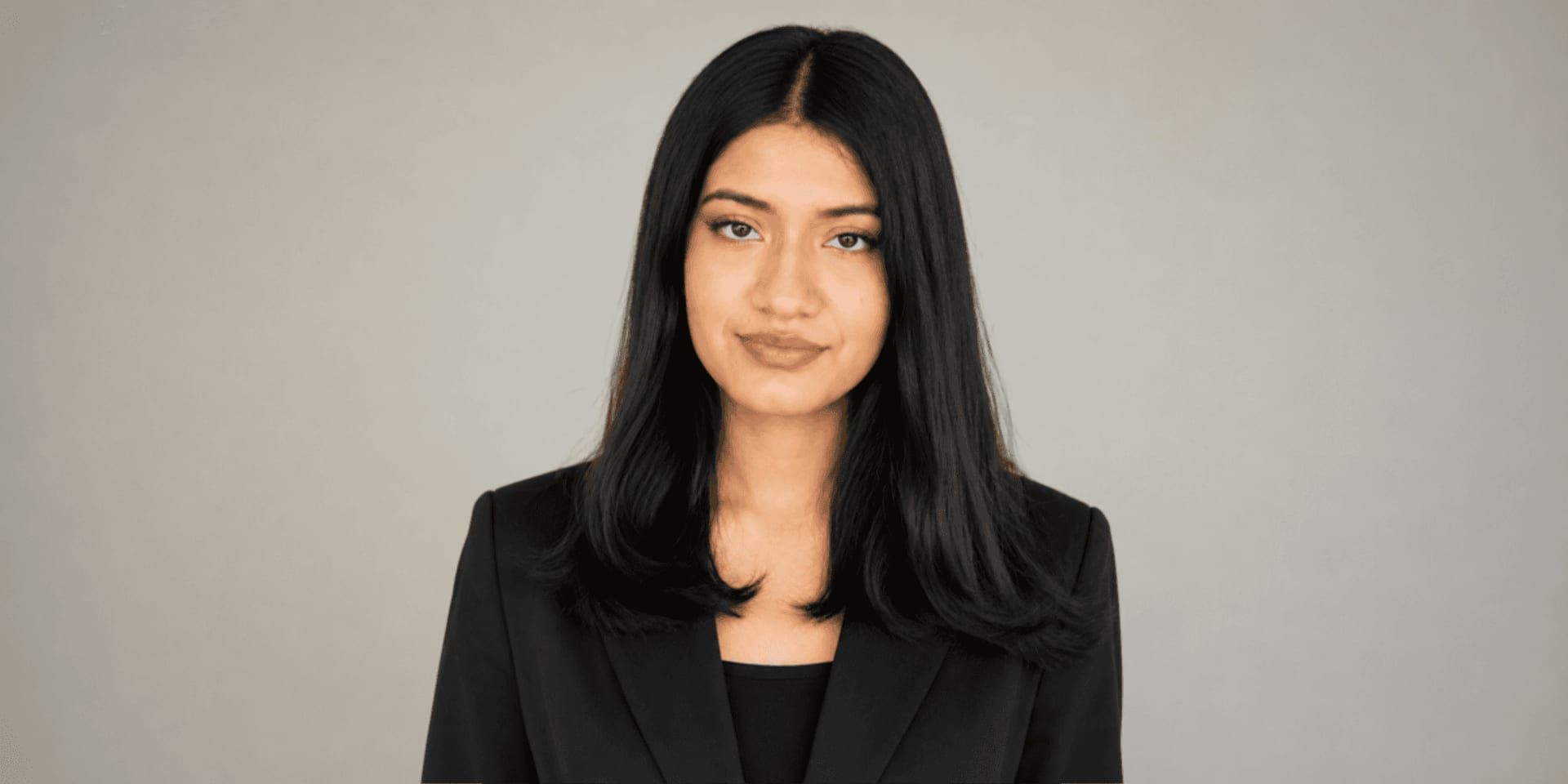 Professional portrait of Yumna Waheed wearing a black blazer against a neutral gray background.