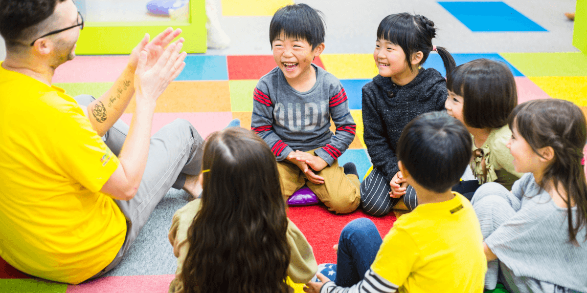 A teacher engaging with a group of smiling young children, fostering a fun, creative learning environment at ABCDAVID’s English School.