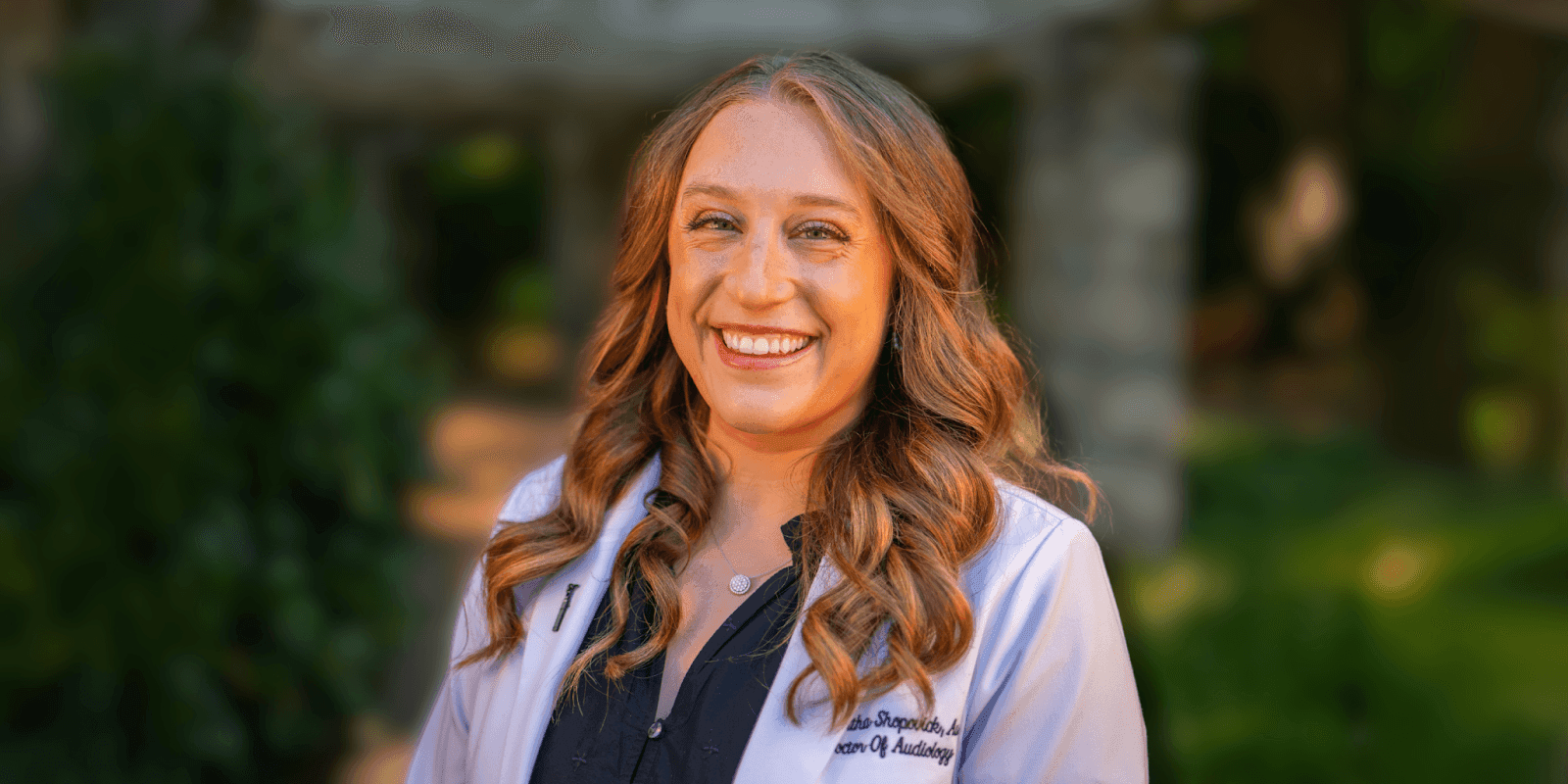 Dr. Samantha Shopovick, Audiologist at Now Hear This® Hearing Aids & Audiology, smiles in a professional setting, showcasing her expertise in personalized audiologic care and hearing aid services in Raleigh, NC