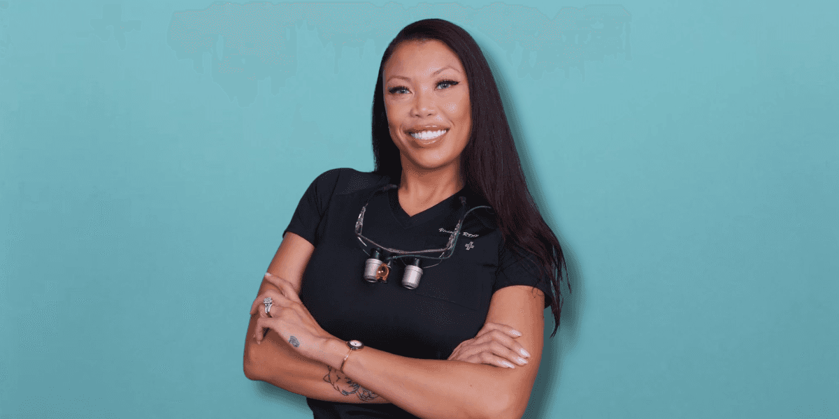 Vivienne Frederiksen RDH wearing dental loupes and black scrubs against a teal background.