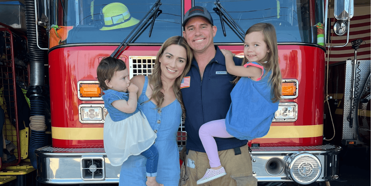 Family poses in front of a fire truck, smiling with two young children.