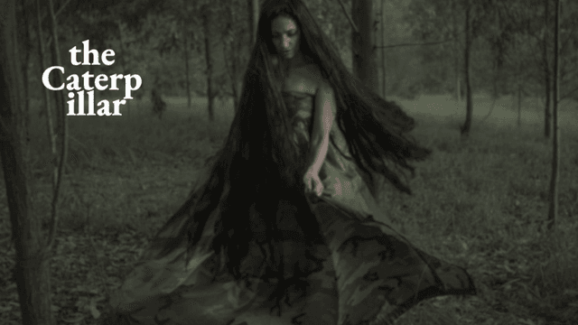 A woman in a camouflage dress stands in a forest with long hair flowing.