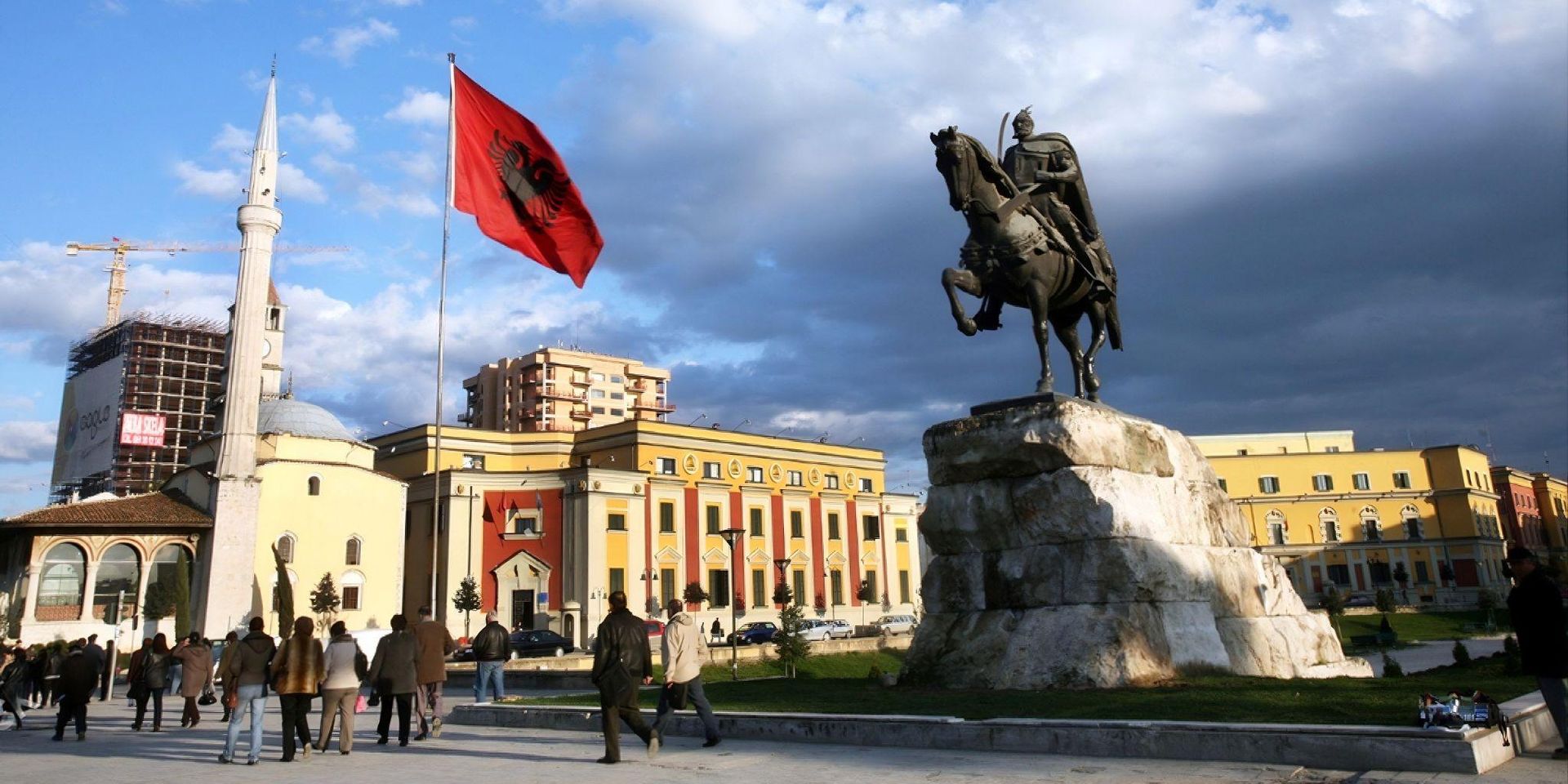 Statue of a knight on horseback in a bustling square with an Albanian flag