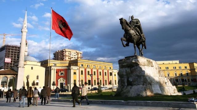 Statue of a knight on horseback in a bustling square with an Albanian flag