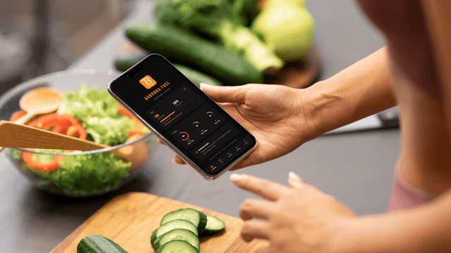 A person using a smartphone while preparing a fresh vegetable salad in a kitchen.