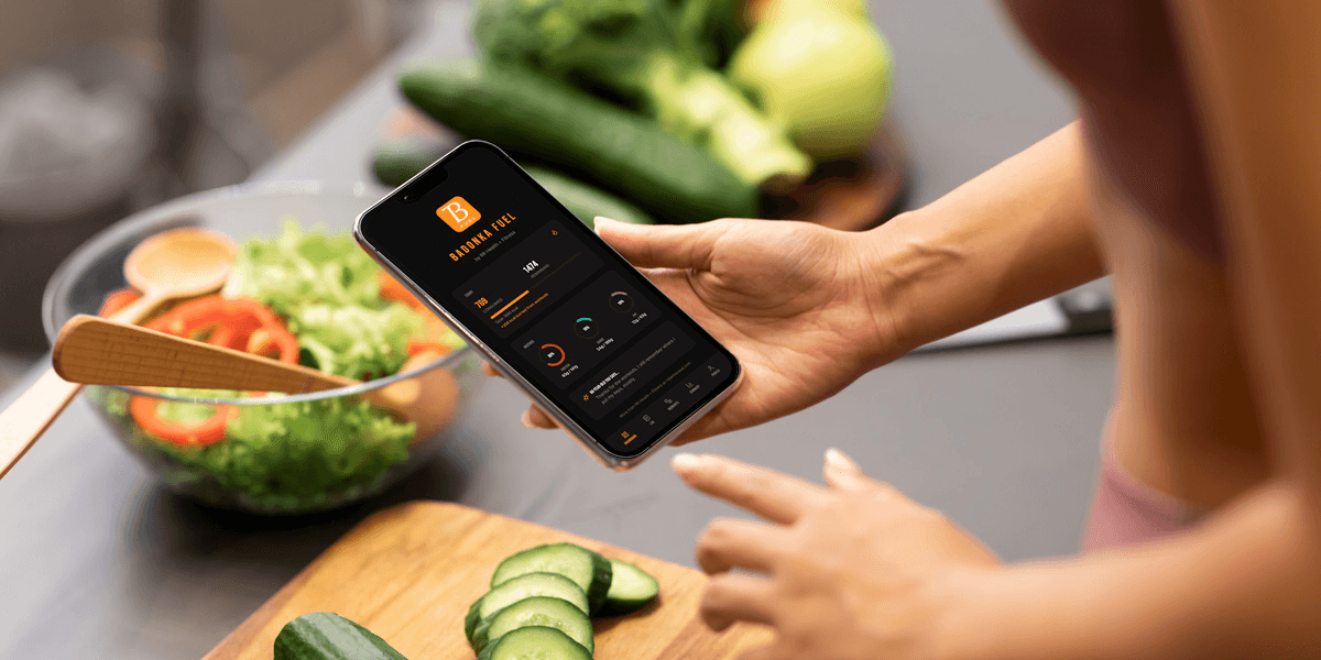 A person using a smartphone while preparing a fresh vegetable salad in a kitchen.