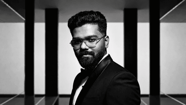 A man in a tuxedo poses confidently against a geometric black and white background