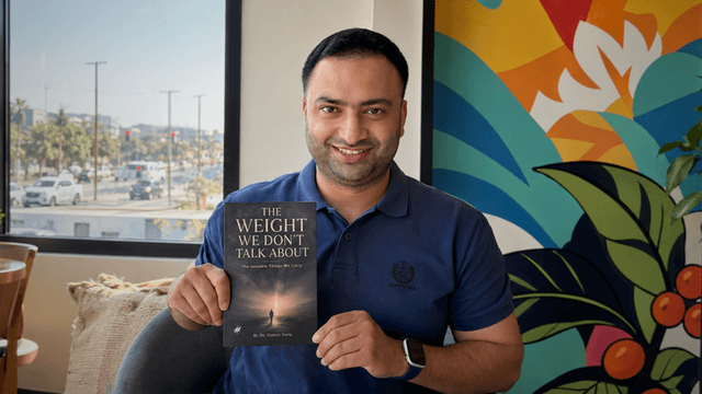 Man holding a book titled "The Weight We Don't Talk About" in a bright cafe setting