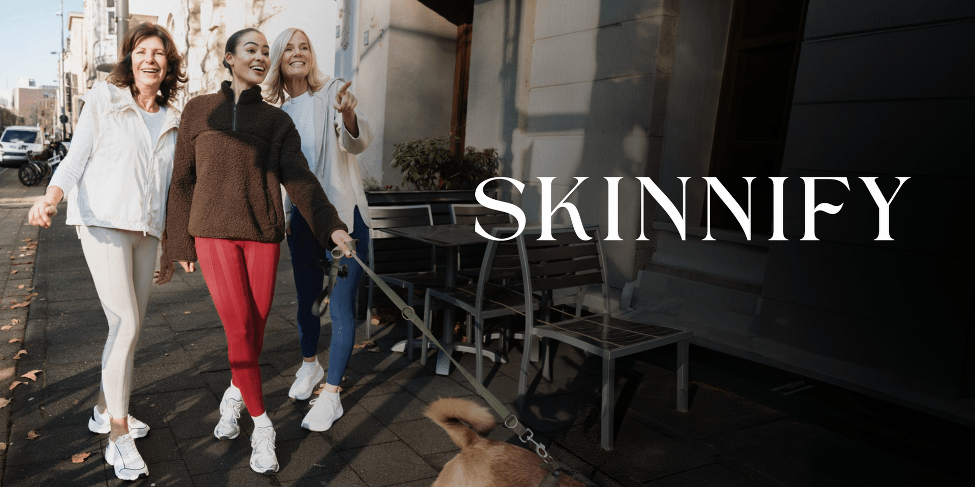 Three women walking a dog on a city street in activewear.