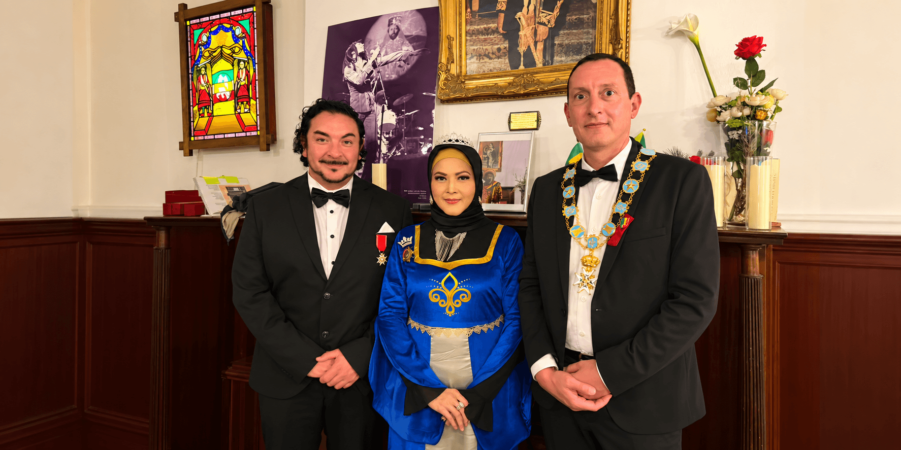 Three individuals in formal attire posed indoors with decorations and a historical backdrop