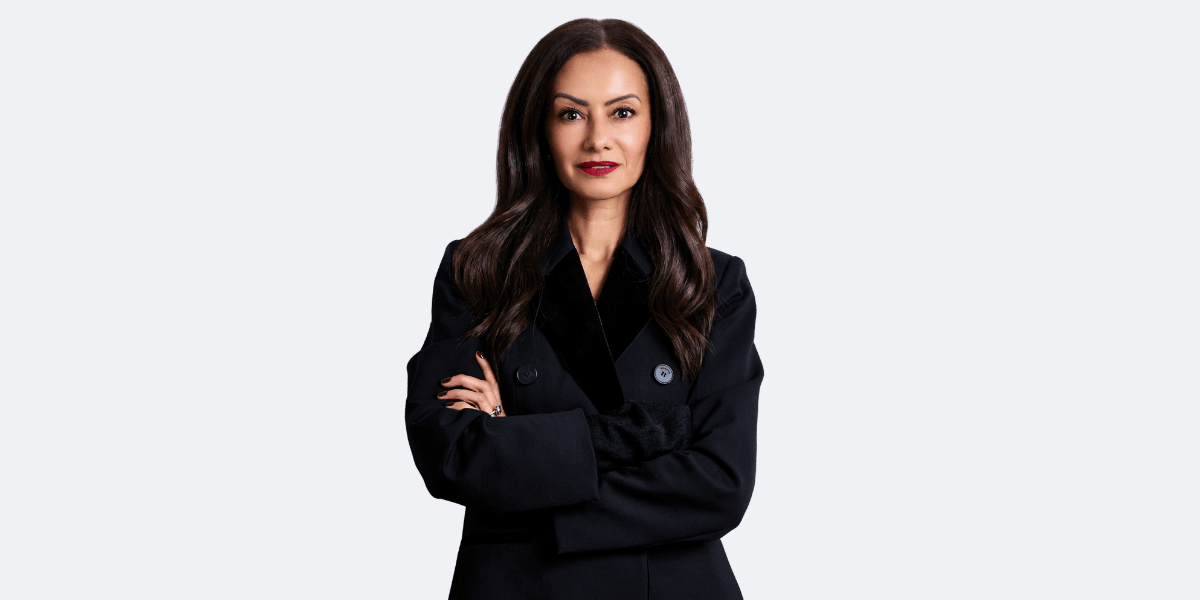Professional woman in a black coat, arms crossed, with long dark hair