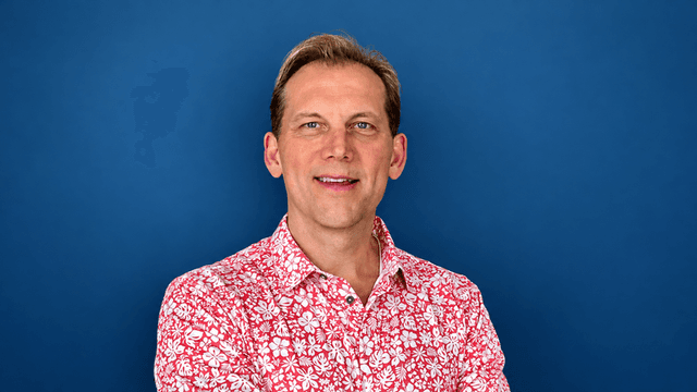 Smiling man in a floral shirt against a blue background