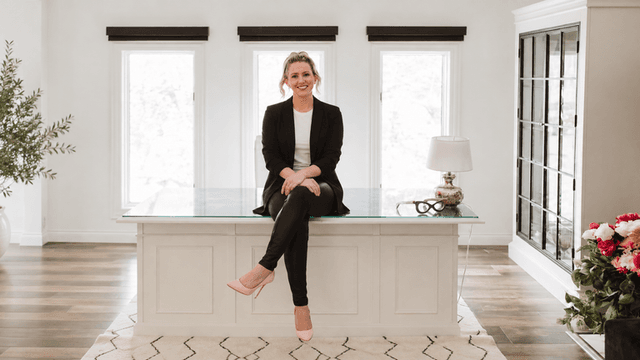Woman in business attire seated on a desk in a bright, modern office space