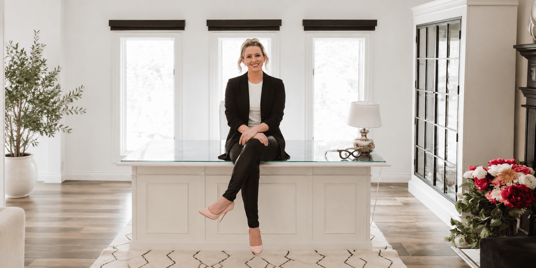 Woman in business attire seated on a desk in a bright, modern office space