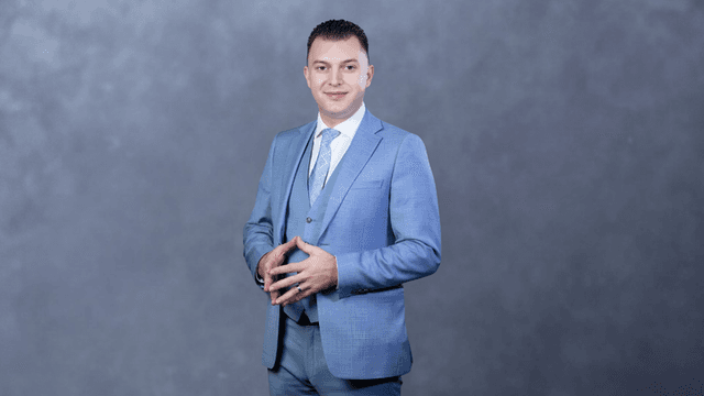 Man in a light blue suit stands confidently against a gray background