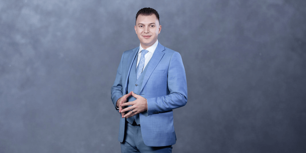Man in a light blue suit stands confidently against a gray background