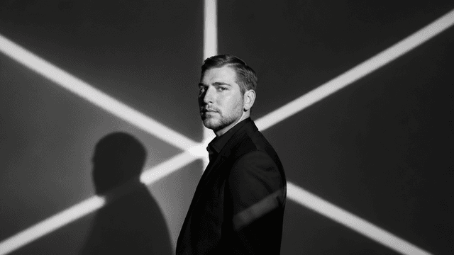 A man in a suit poses against a stark black and white background with shadows