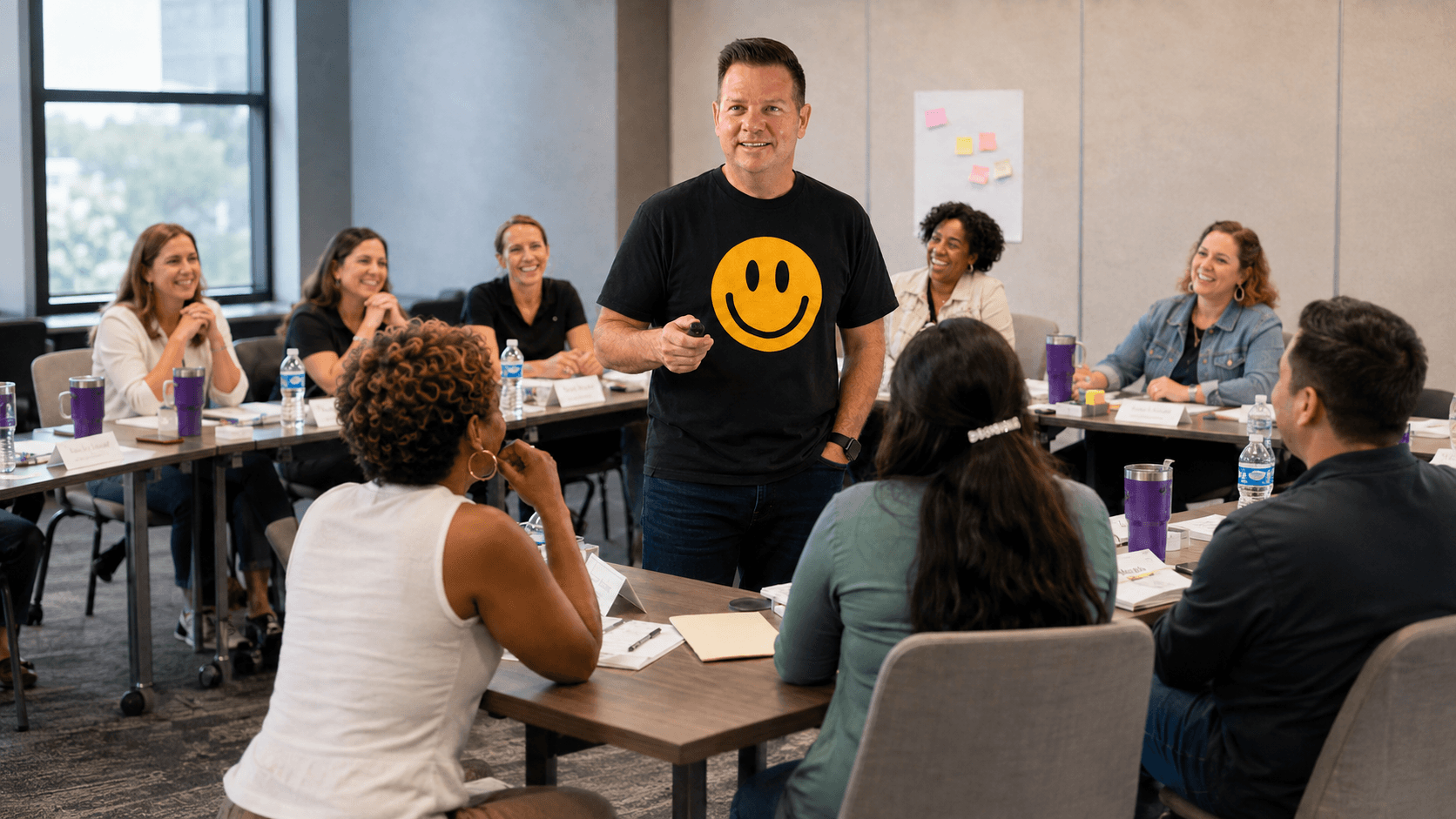 A smiling speaker in a t-shirt engages a diverse group in a meeting room