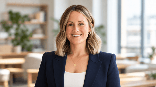 Smiling woman with shoulder-length hair wearing a blazer in a bright, modern setting