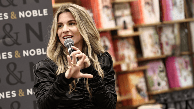 A woman with long hair speaking into a microphone at a bookstore event