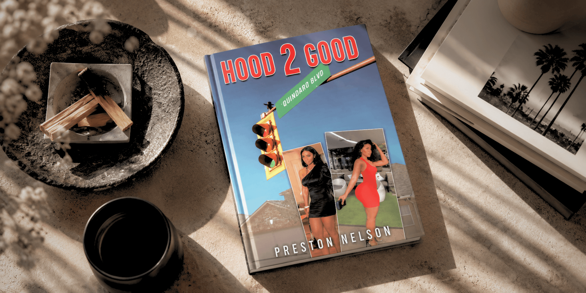 A book titled "Hood 2 Good" on a textured surface with decorative items nearby