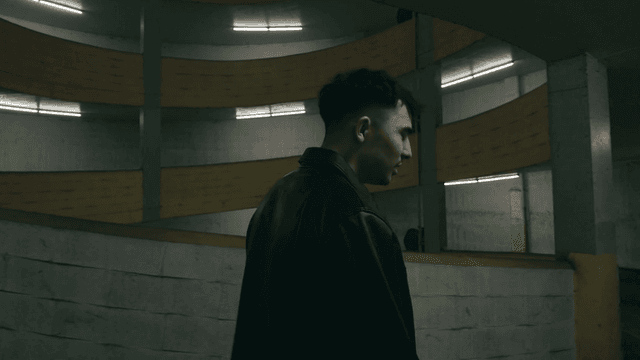 A person in a leather jacket stands in a dimly lit parking garage.
