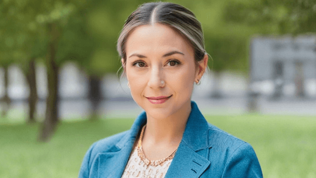 Woman with a light blue blazer and gold necklace in a green park setting