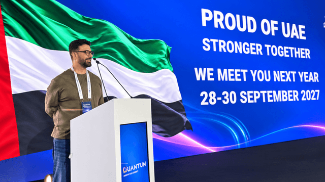 A speaker addresses an audience with a UAE flag backdrop and event details displayed.