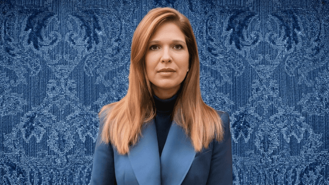 A woman with long, straight hair wearing a blue blazer against a patterned blue background