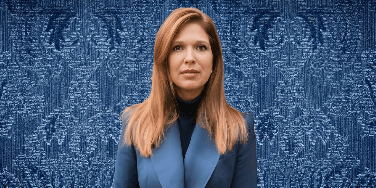 A woman with long, straight hair wearing a blue blazer against a patterned blue background