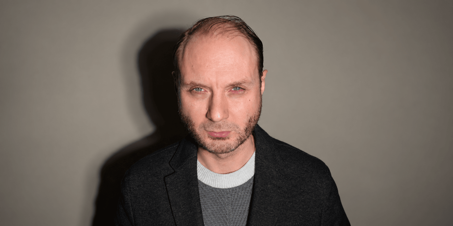 A man with short hair and a serious expression, wearing a dark jacket.