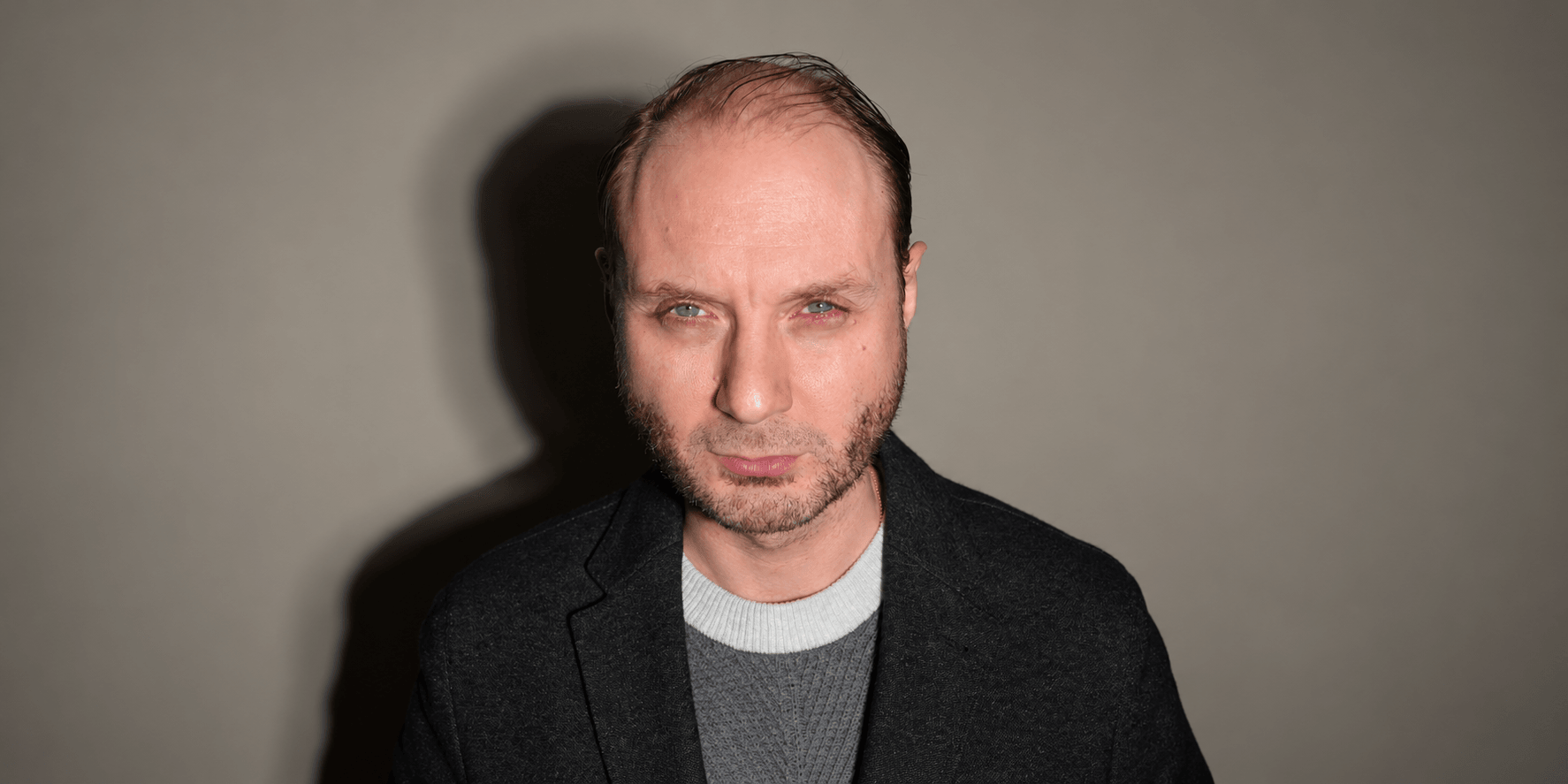 A man with short hair and a serious expression, wearing a dark jacket.