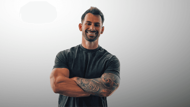 Smiling man with tattoos, crossed arms, wearing a fitted black shirt
