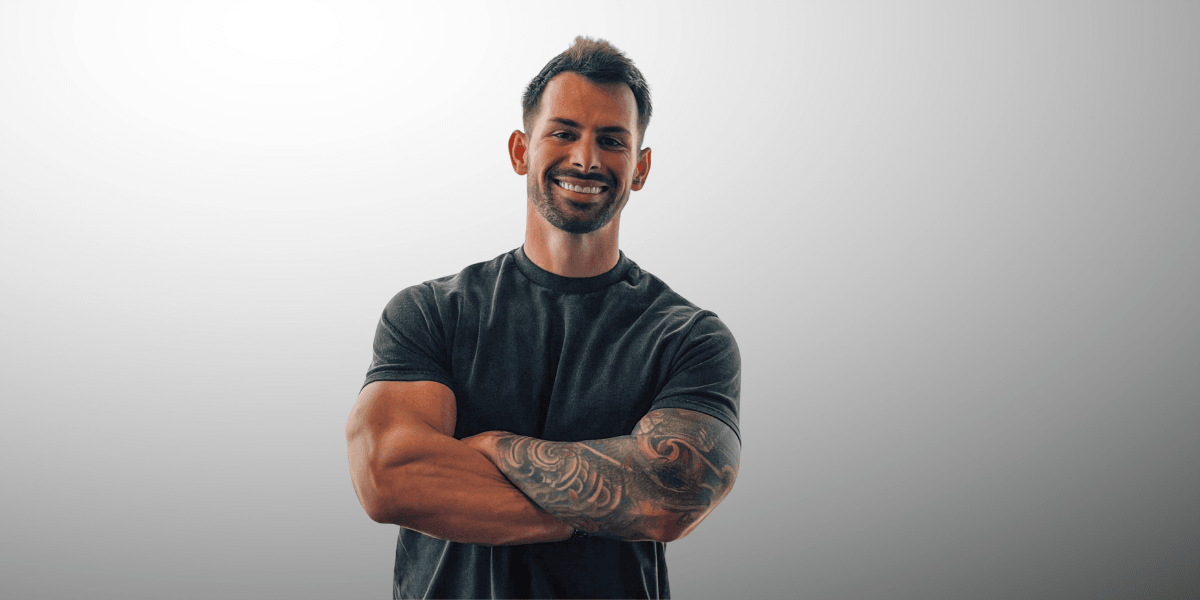 Smiling man with tattoos, crossed arms, wearing a fitted black shirt