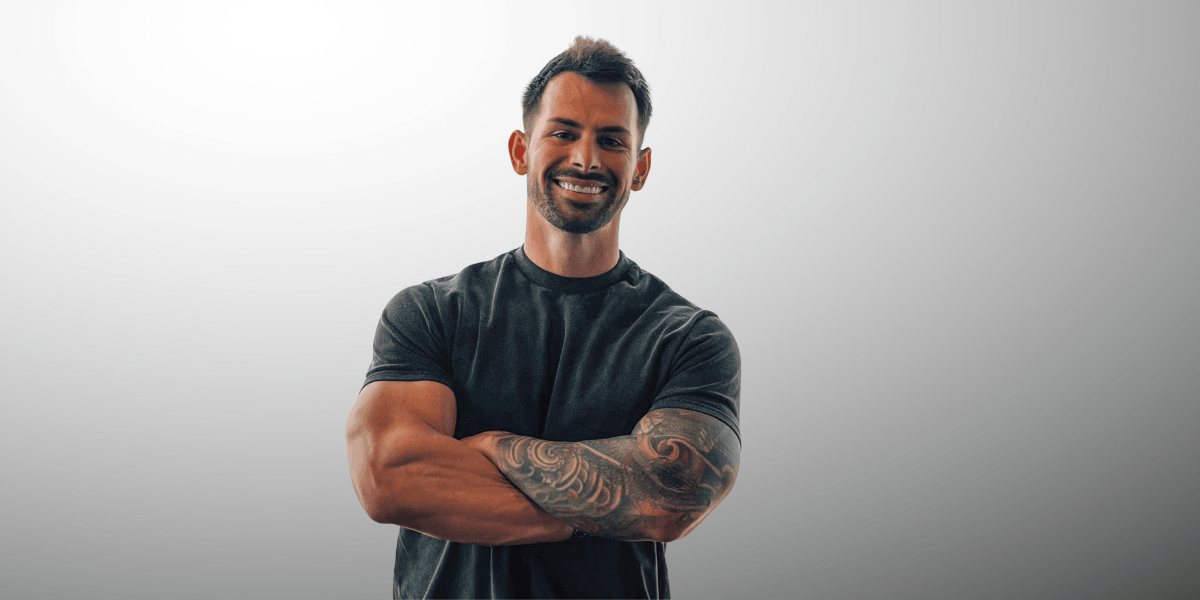 Smiling man with tattoos, crossed arms, wearing a fitted black shirt