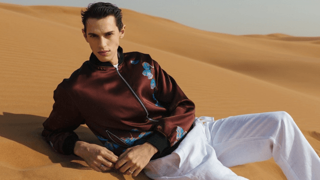 Male model in a desert wearing a patterned bomber jacket and white pants