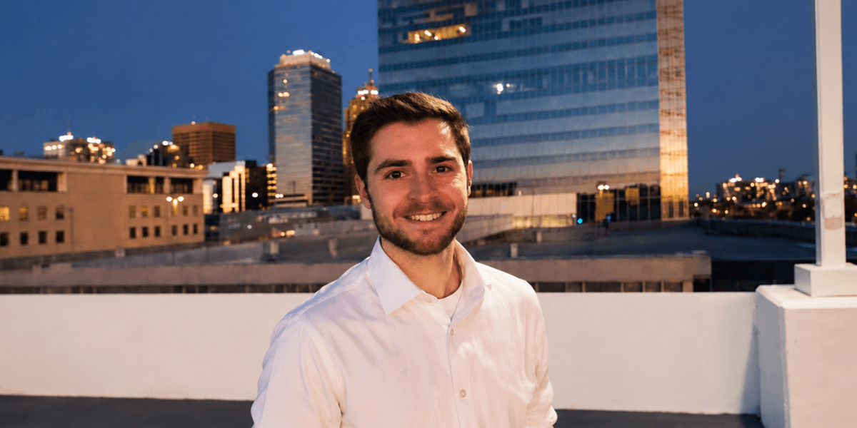 Smiling man in a white shirt against a city skyline at dusk