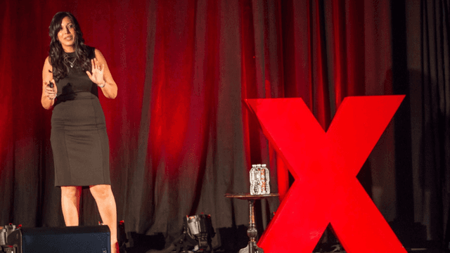 Woman speaking on stage beside a large red TEDx logo and water bottles