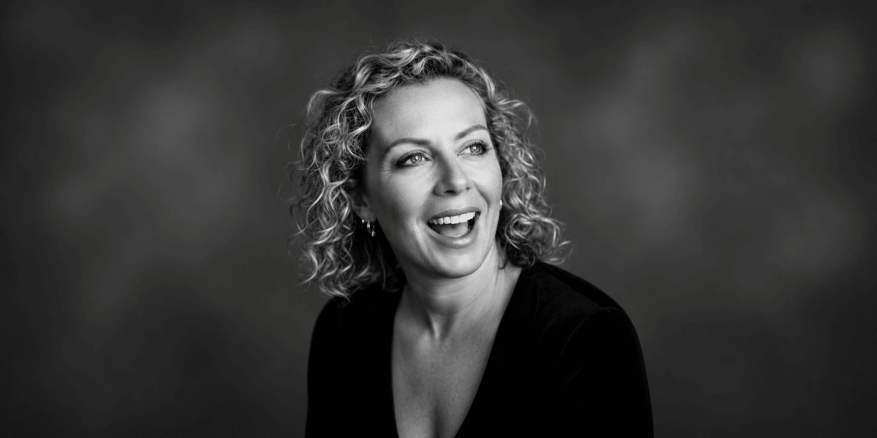 Woman with curly hair smiling, wearing a black top against a blurred background