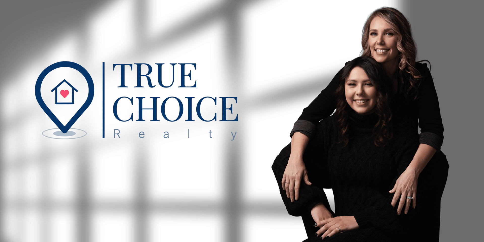 Two women posing together in front of a logo for True Choice Realty