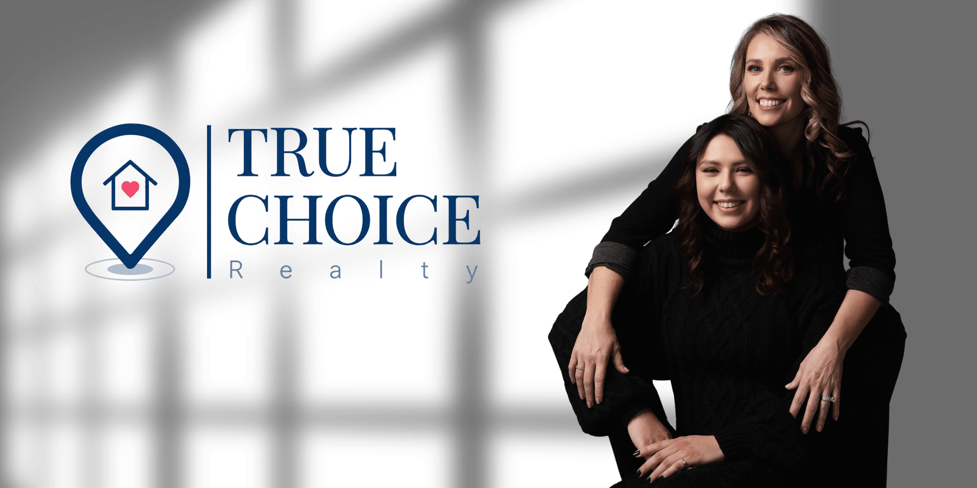 Two women posing together in front of a logo for True Choice Realty