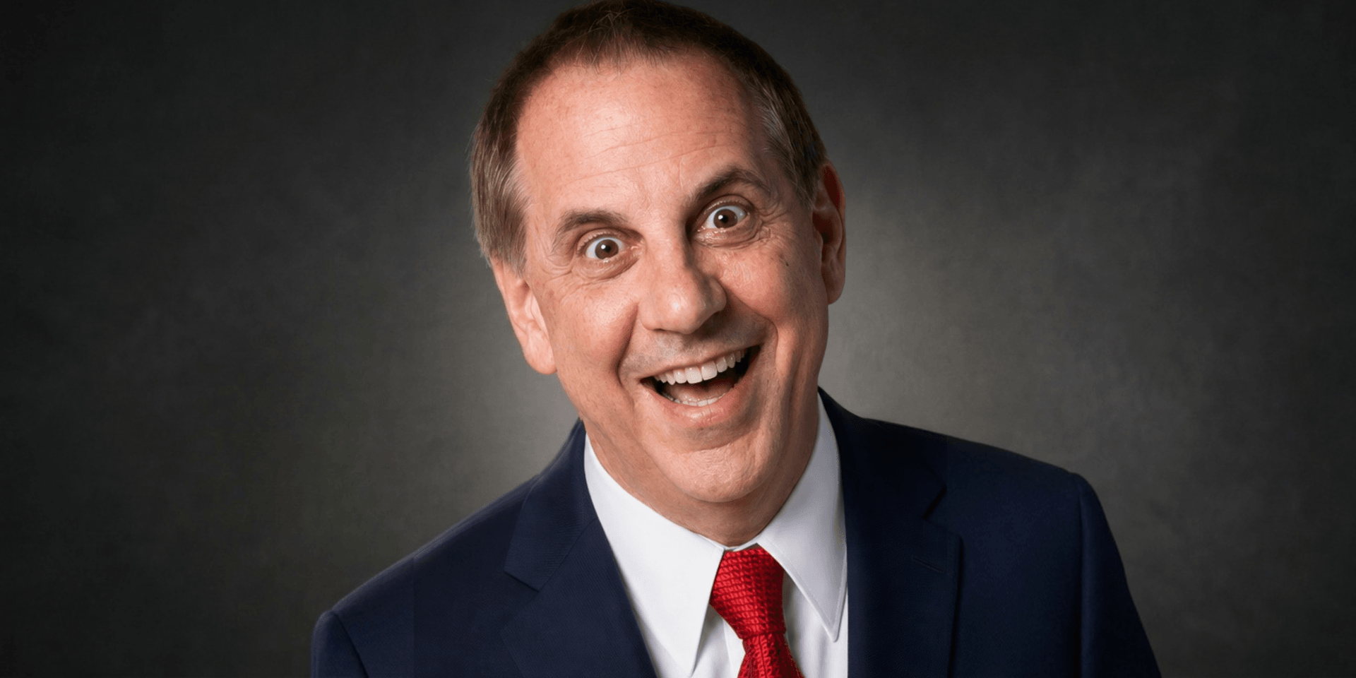Smiling man in a suit with a red tie against a dark background
