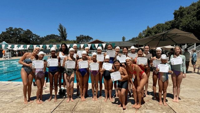 Group of young swimmers proudly holding certificates by a pool on a sunny day