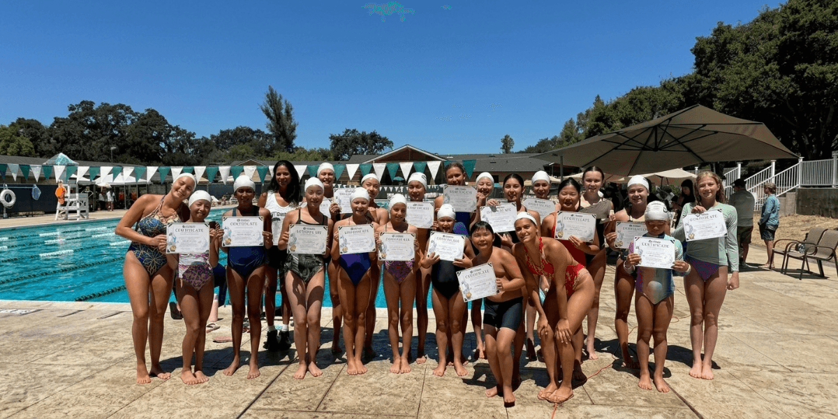 Group of young swimmers proudly holding certificates by a pool on a sunny day