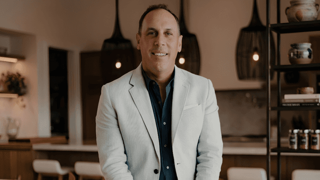 Man in a light suit stands confidently in a modern kitchen setting