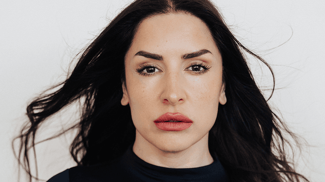 A woman with long dark hair and full lips gazes directly at the camera