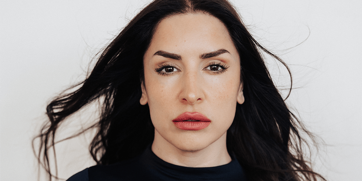 A woman with long dark hair and full lips gazes directly at the camera